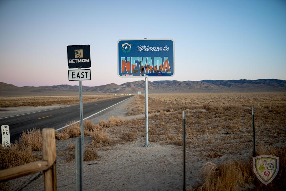 A "Welcome to Nevada" road sign is seen on a stretch of highway in the desert. Next to it is another road sign with the BetMGM logo, indicating signs that the poker operator may soon launch its product there.